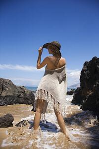Young adult female Caucasian standing in water on beach tilting brimmed hat.
