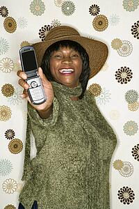 African-American mid-adult woman in front of vintage pattern background holding out cellphone.