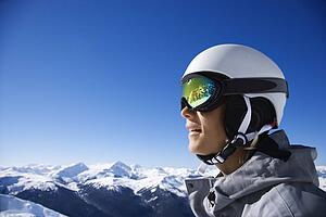 Caucasian teenage boy snowboarder wearing helmet and goggles on mountain.