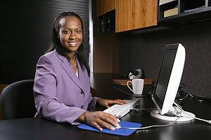 African-American young adult business woman working at computer in office smiling and looking at viewer.