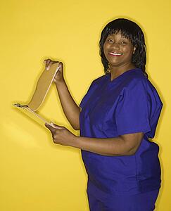 African-American mid-adult woman in medical uniform smiling reading chart.
