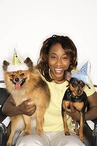 African American young adult female holding brown Pomeranian and Miniature Pinscher dogs wearing party hats.
