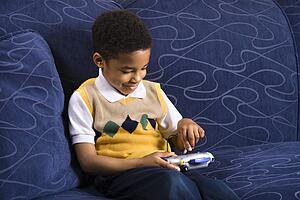 Portrait of young boy playing video game on couch. 
