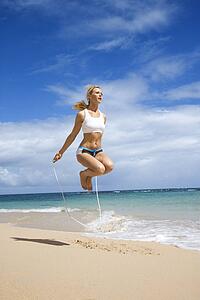 Caucasian young adult woman jumping rope on beach.