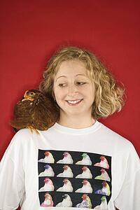 Caucasian mid-adult woman looking at chicken on shoulder.
