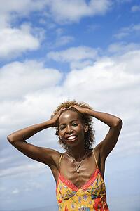 Mid-adult Black female with hands on forehead with clouds in background.
