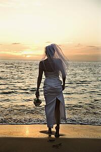 Young adult female Caucasian bride standing on beach at sunset.