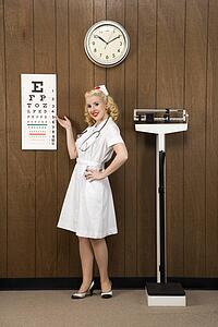 Caucasian mid-adult female nurse pointing to eye chart and looking at viewer.