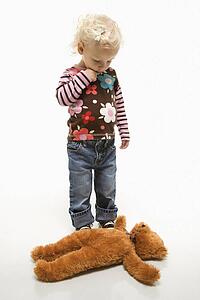 Young Caucasian female toddler looking at her teddy bear on ground.