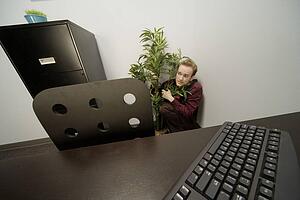 Businessman hiding behind a potted plant in an office