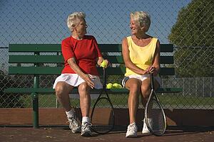 Two senior women sitting with tennis rackets