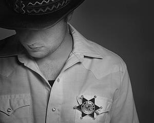 Cowboy looking down under hat with Sheriff's badge on shirt