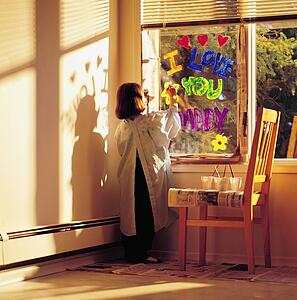 Little girl painting 'i love you daddy' on window