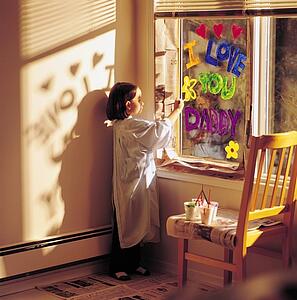Little girl painting 'I love you daddy' on window
