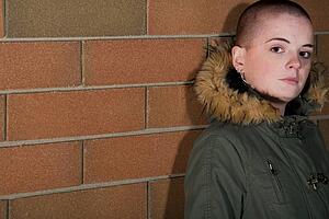 Teen girl with shaved head standing against brick wall
