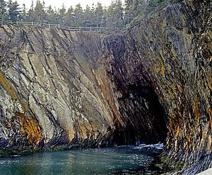 A rock wall leading into a cave with water flowing into it
