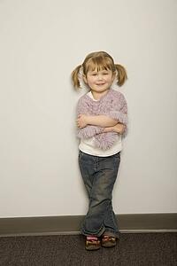 Smiling little girl leaning against a wall with arms crossed