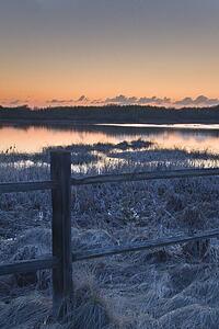 Fence by lake at sunset