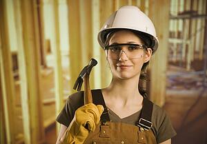 A woman wearing construction hat and holding a hammer