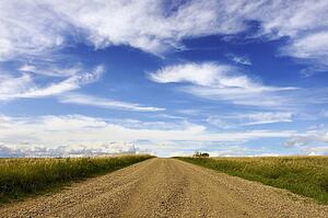 Gravel road with fields and white clouds