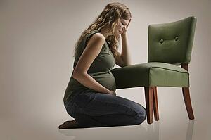 A sad pregnant woman sitting by chair