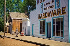 Woman in period dress walking past historic hardware store at Fort Edmonton Park 