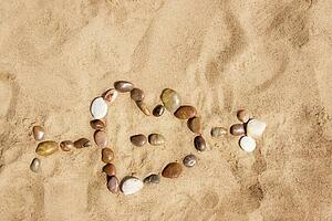 Heart pierced by cupid's arrow made out of stones and placed on sand