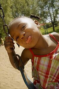 Young girl sticking out her tongue while on the swing set at the park
