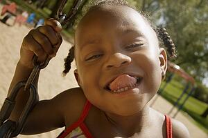 Young girl sticking out her tongue while on the swingset in the park