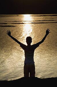 Child stretching arms to the sky at river bank
