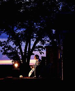 Man sitting with guitar by lantern at dusk