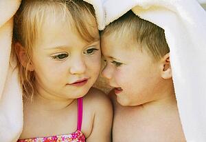 Two kids snuggle under a towel
