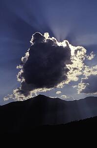 Sun behind a cloud above mountain range