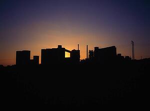 Concrete factory silhouette, backlit by the sun on the horizon