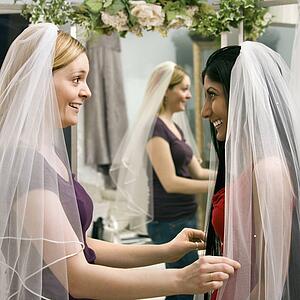 Indian woman and Caucasian woman trying on veils and looking in mirror.