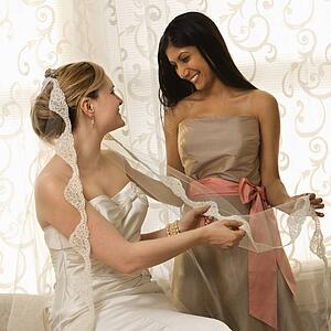 Indian maid of honor holding Caucasian bride's veil.