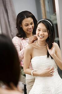 Friend helping place necklace on bride