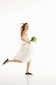 Caucasian bride running and holding bouquet.