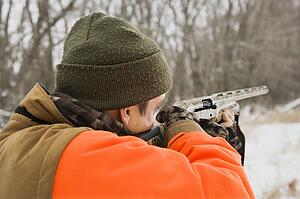 Male aiming shotgun out towards woods