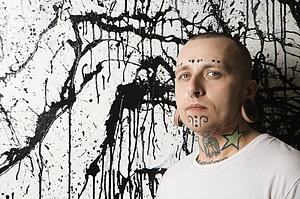 Tattooed and pierced man against paint splattered background
