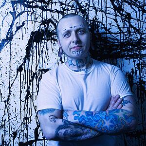 Tattooed and pierced man standing against paint splattered background.
