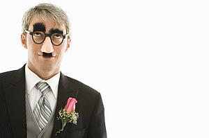 Caucasian groom wearing groucho glasses looking up.