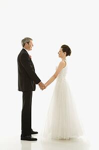 Portrait of Caucasian groom and Asian bride holding hands.