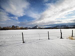 Barbed wire fence with snow covered ground and mountains in background