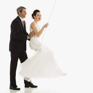Caucasian groom pushing Asian bride in swing set.