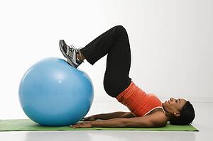 Profile of African American woman stretching on mat with feet on exercise ball.