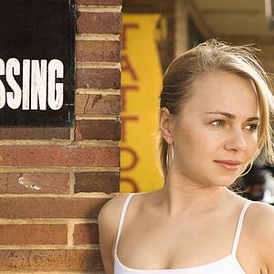 Attractive young Caucasian woman standing outside tattoo parlor.