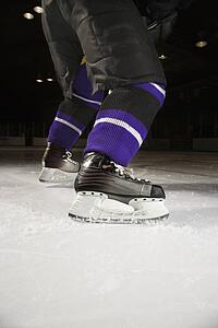 Low angle of hockey player's legs and skates on ice rink.