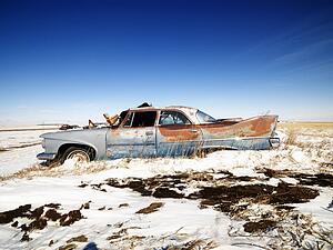 Classic rusted car in snowy junkyard.