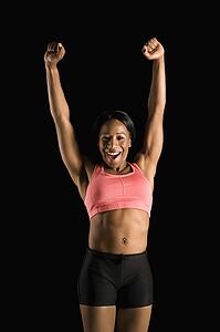 Smiling African American young adult woman in athletic apparel stretching arms above head.